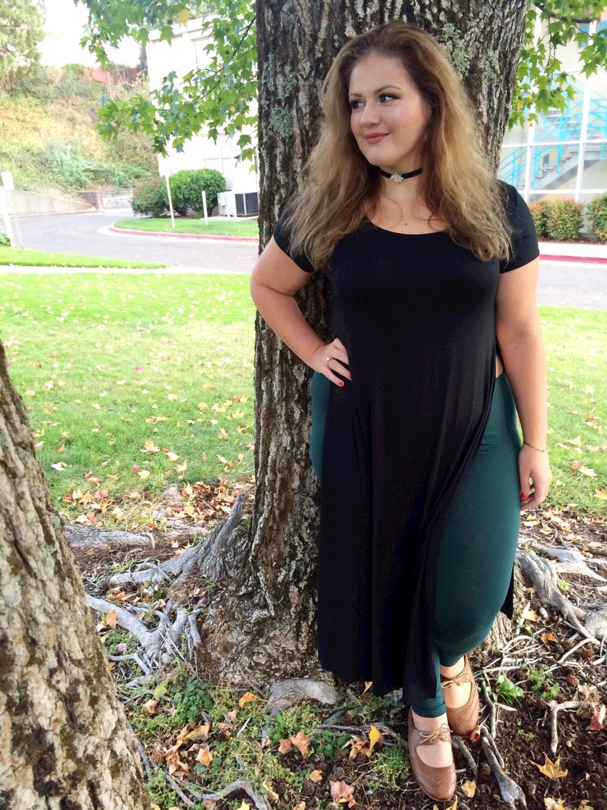 Une belles rondes assez jeune pose devant un arbre dans un parc. C'est une femme avec des rondeurs qui sourit au photographe